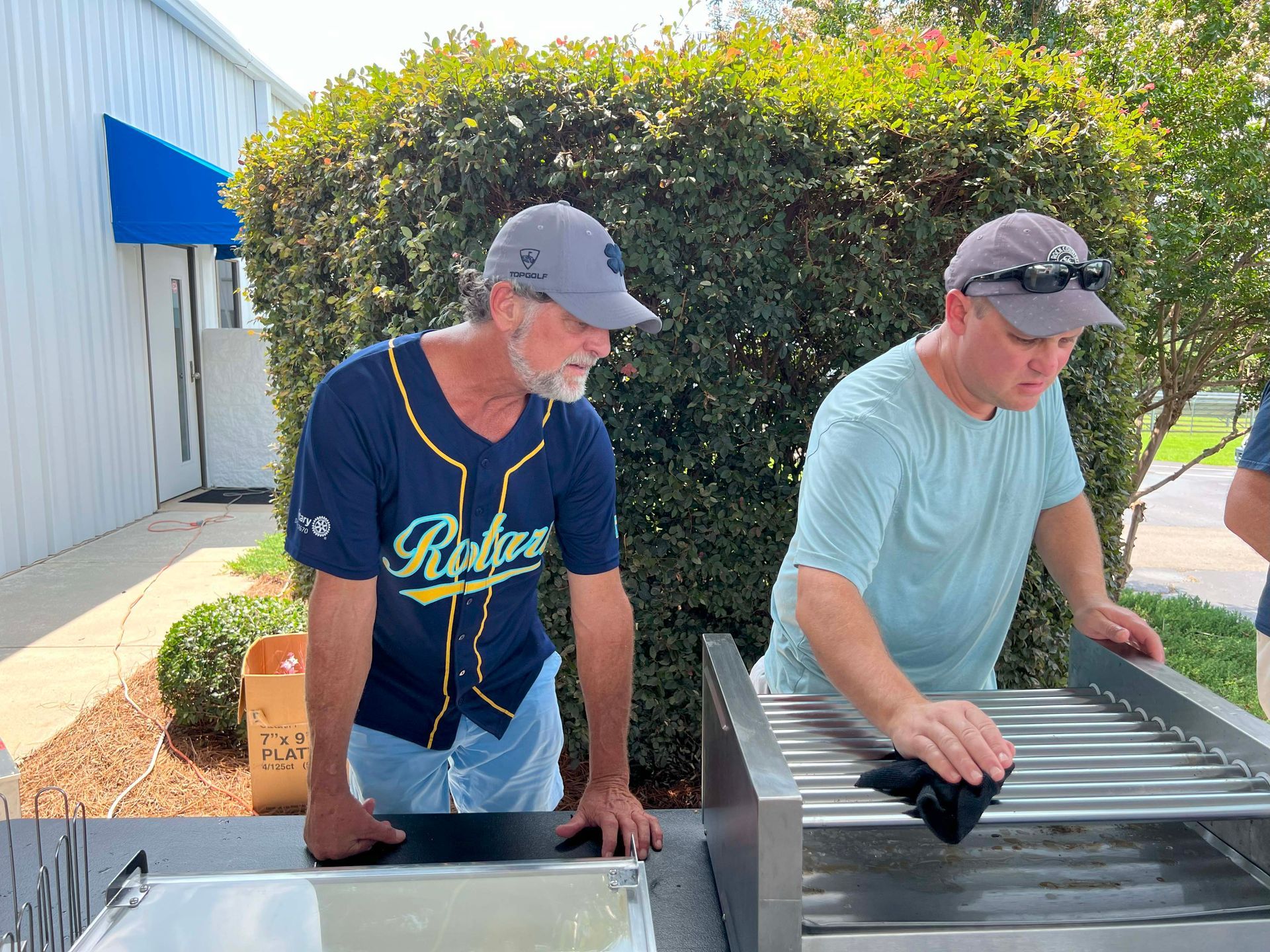 Two men inspecting a metal grill outdoors beside a building