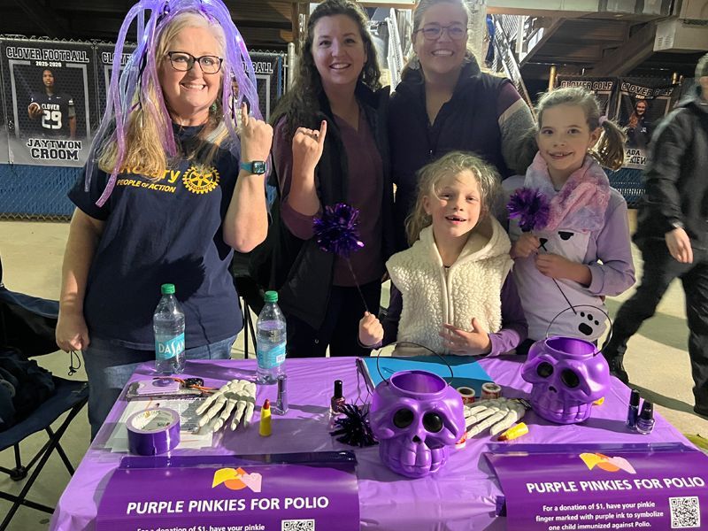 People posing behind a purple “Purple Pinks for Poo” fundraising table with skull decorations and a dog portrait