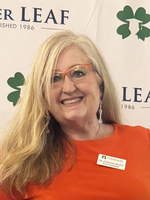 Smiling woman in glasses and orange shirt at a Leaf event backdrop