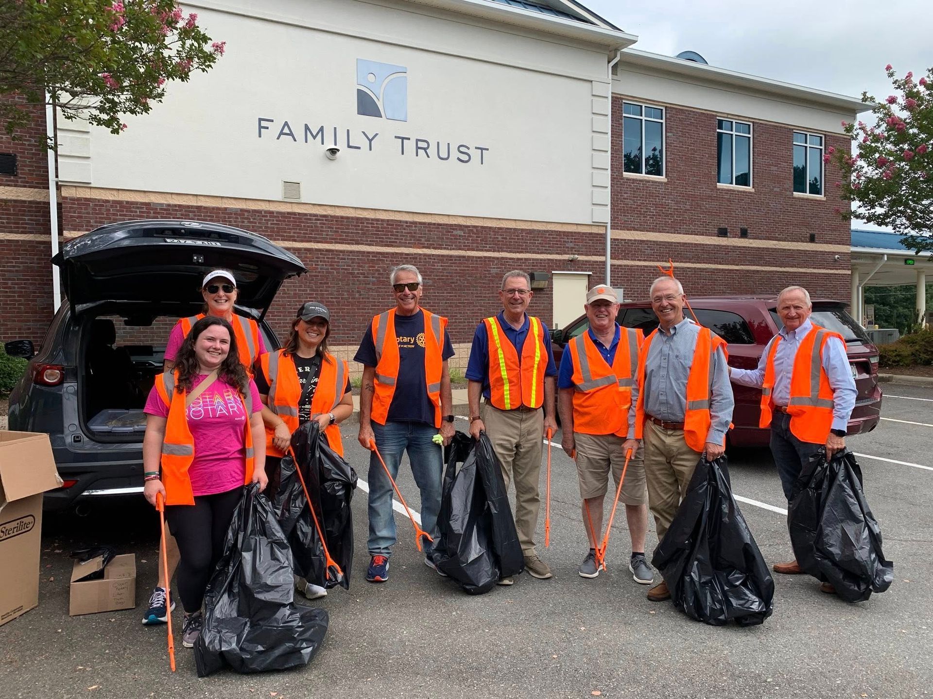 Volunteers in orange safety vests holding trash bags outside Family Trust building during a cleanup event