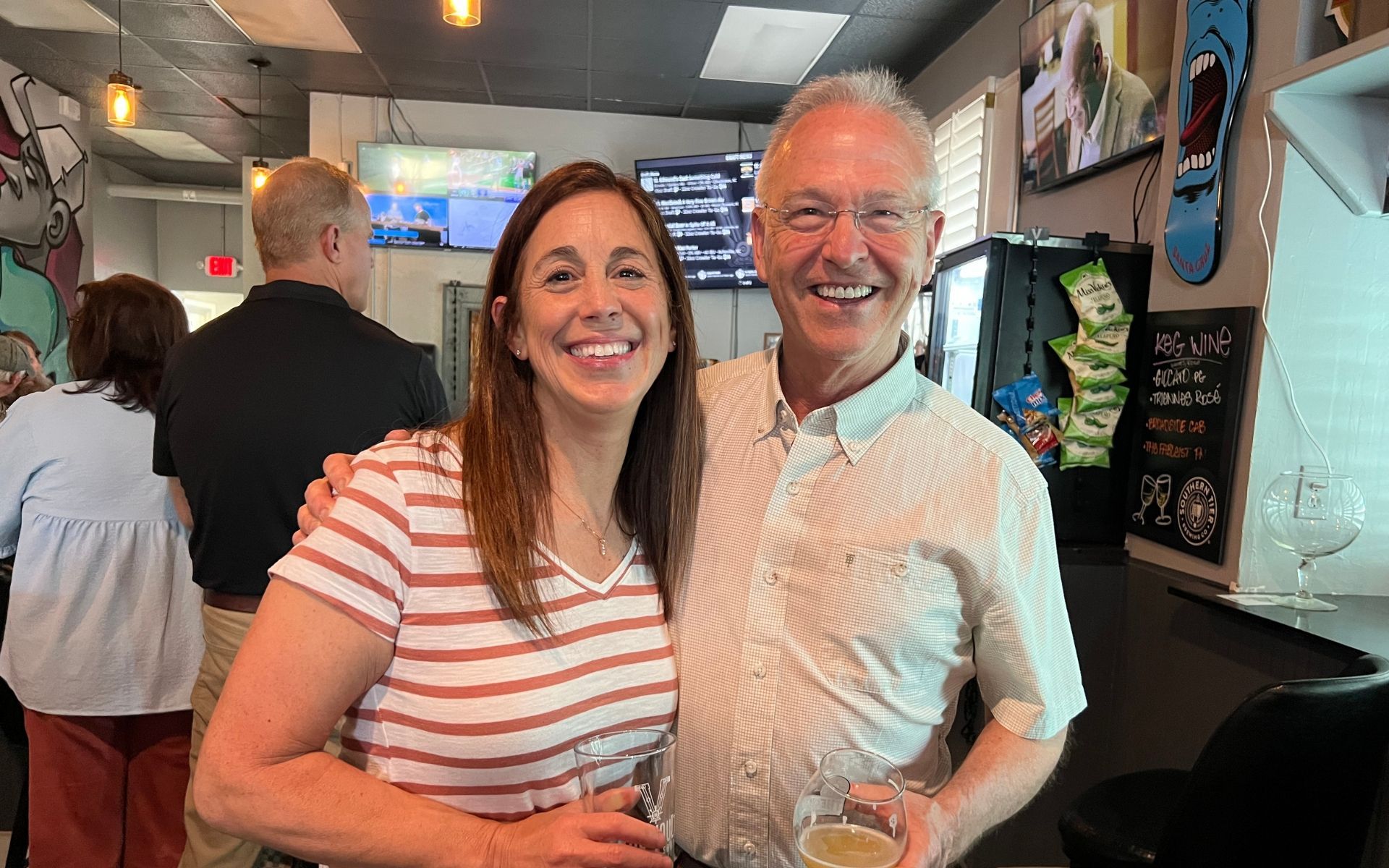 Two smiling people standing in a casual café, posing for a photo.