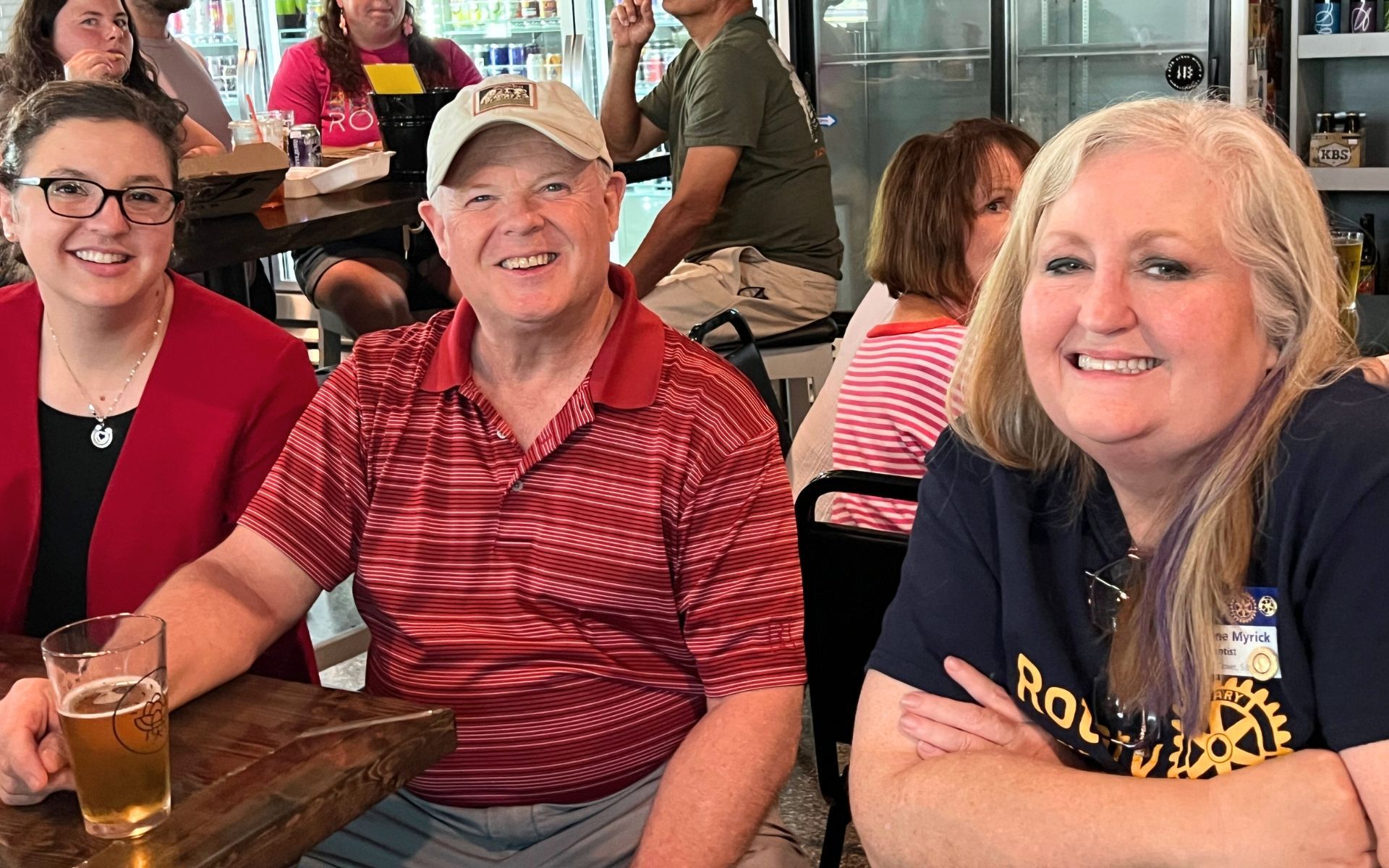 Three smiling people seated at a restaurant table with drinks in a casual dining setting