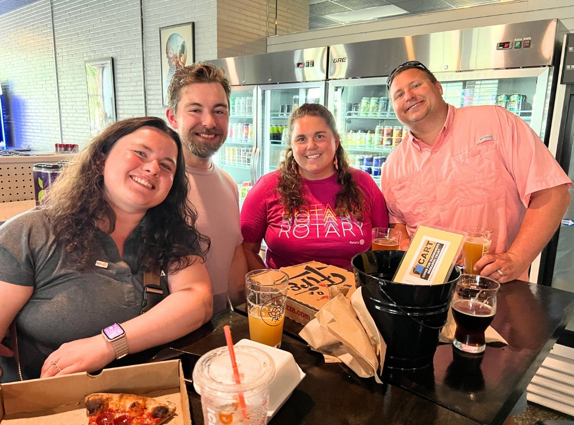 Four friends smiling at a restaurant table with drinks and food trays