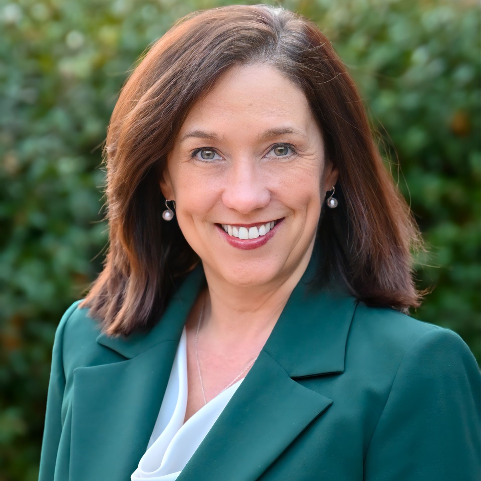 Smiling professional in teal blazer outdoors with blurred greenery background