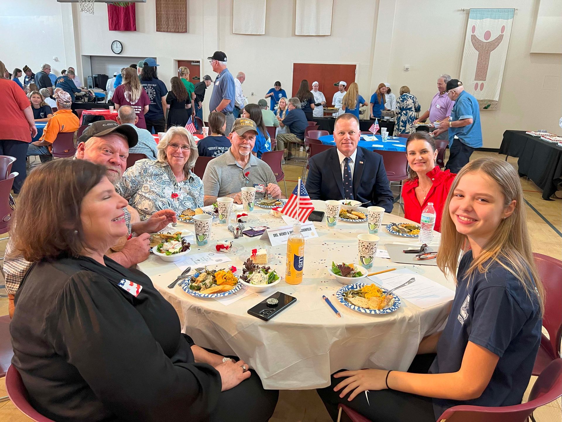 People seated at round tables at a lively community banquet, smiling and eating.