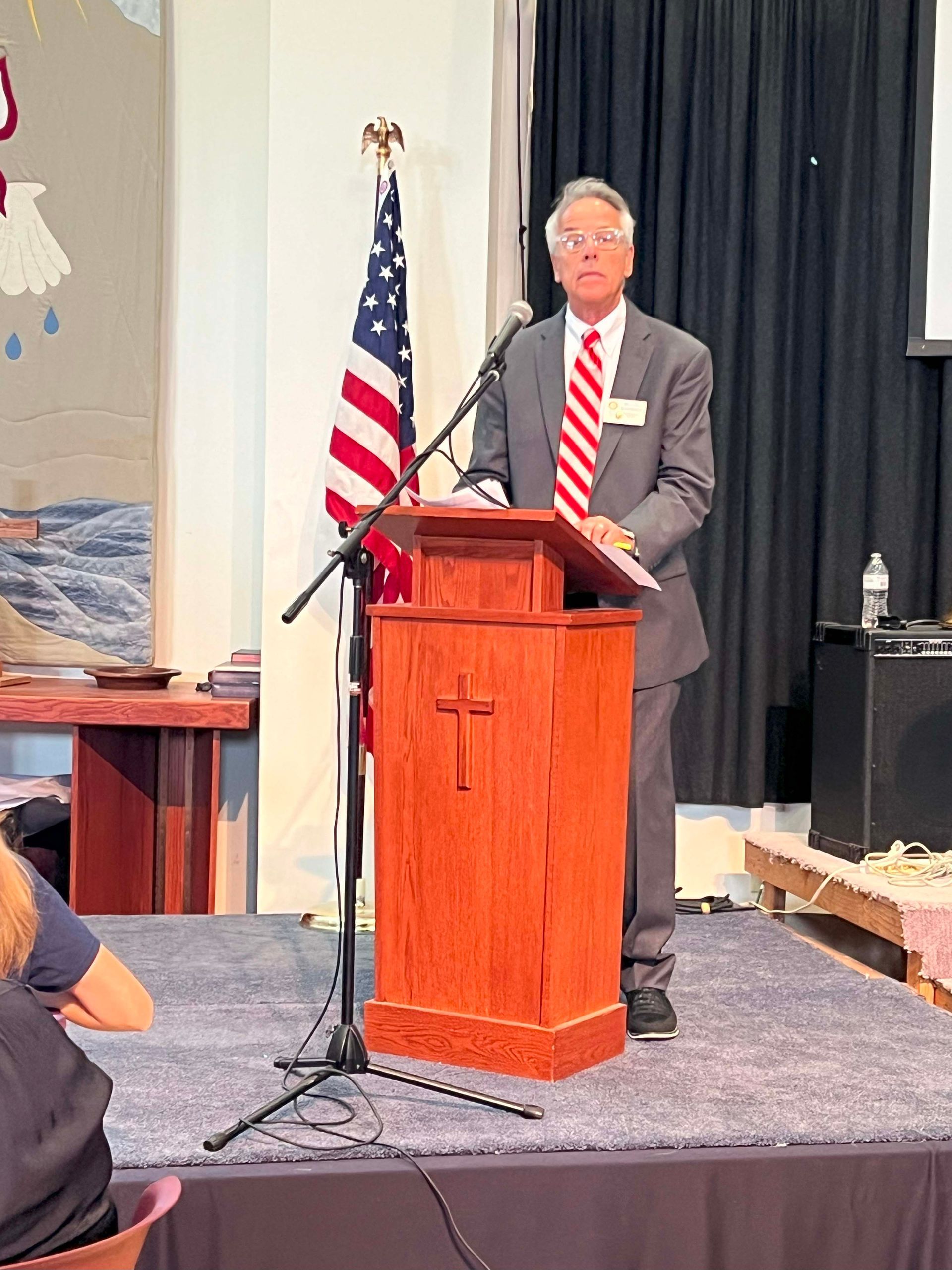 Man speaking at a podium with a U.S. flag beside him on a stage