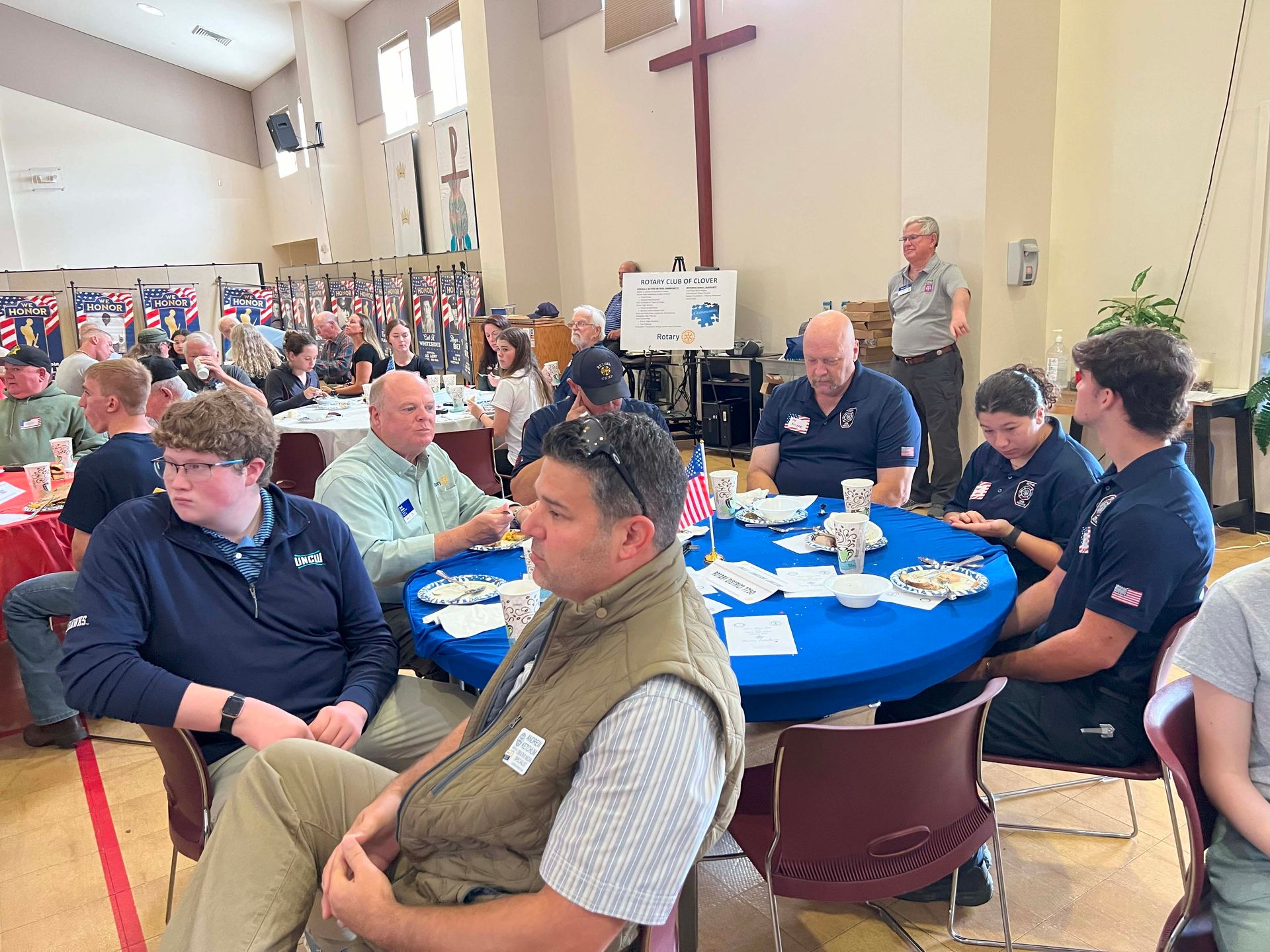 People seated at blue round tables in a church hall during a community gathering