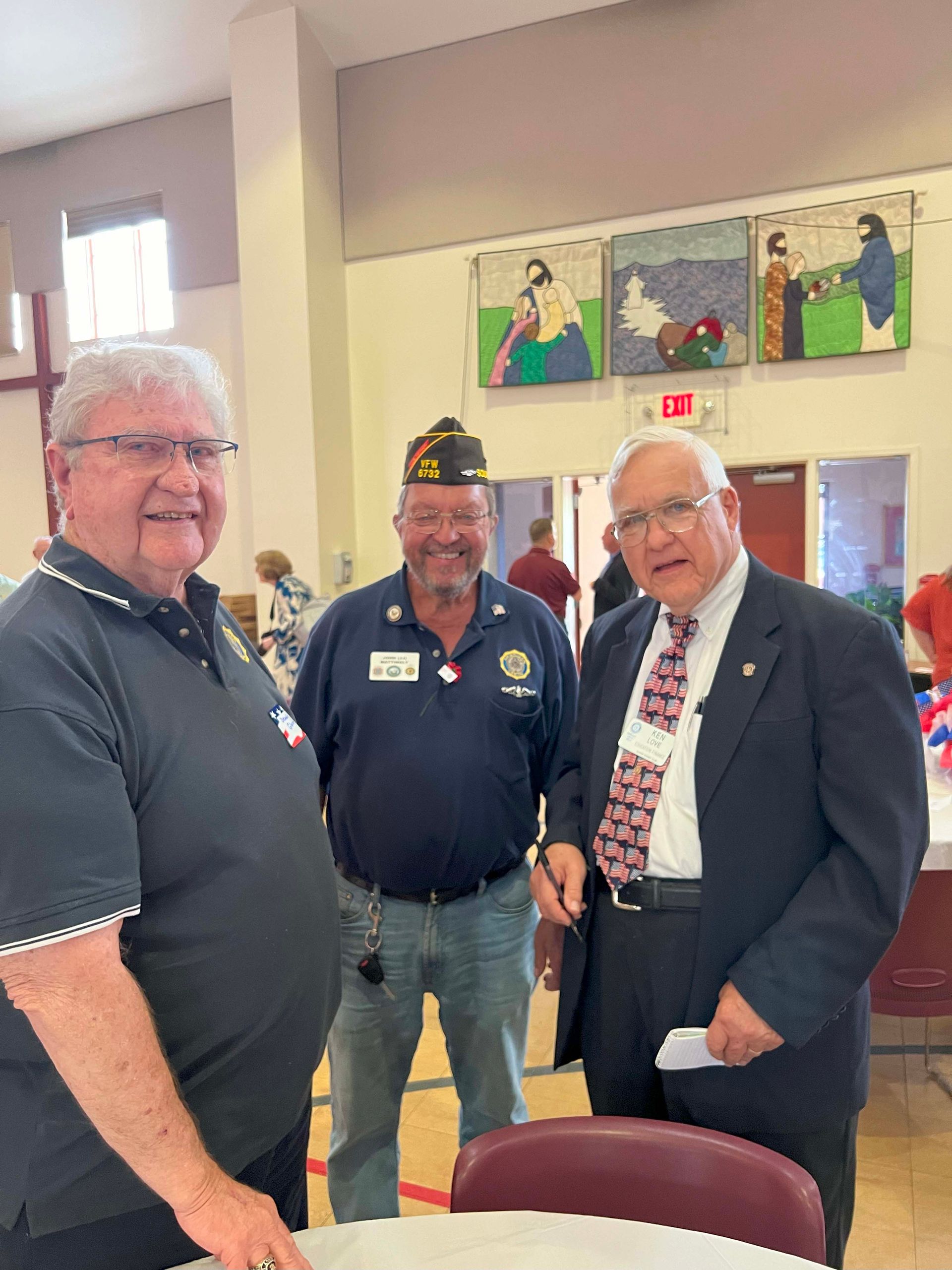 Three men smiling at an indoor event, standing near tables and wall art.