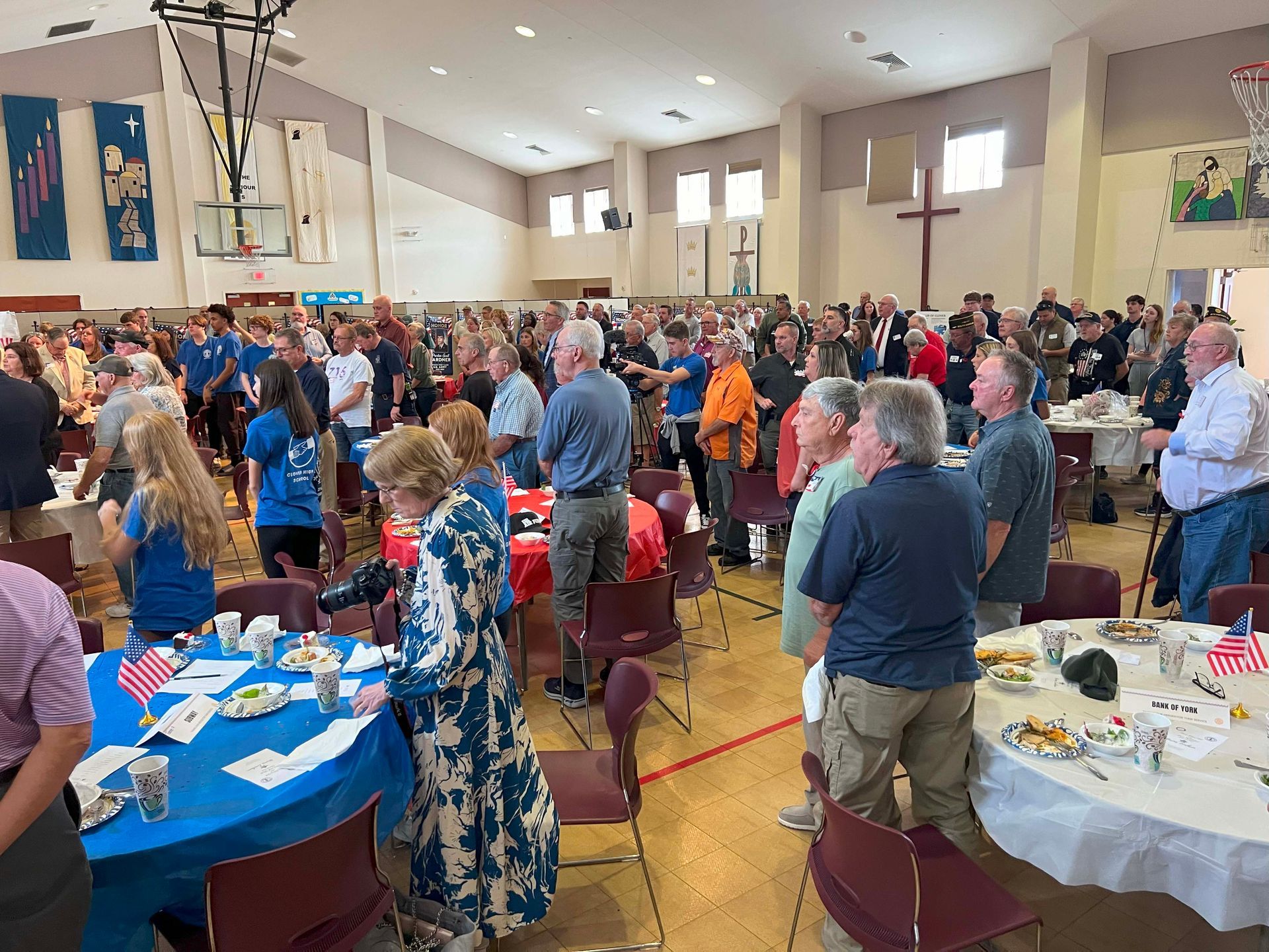 Crowded church hall with people mingling around round tables at a community event
