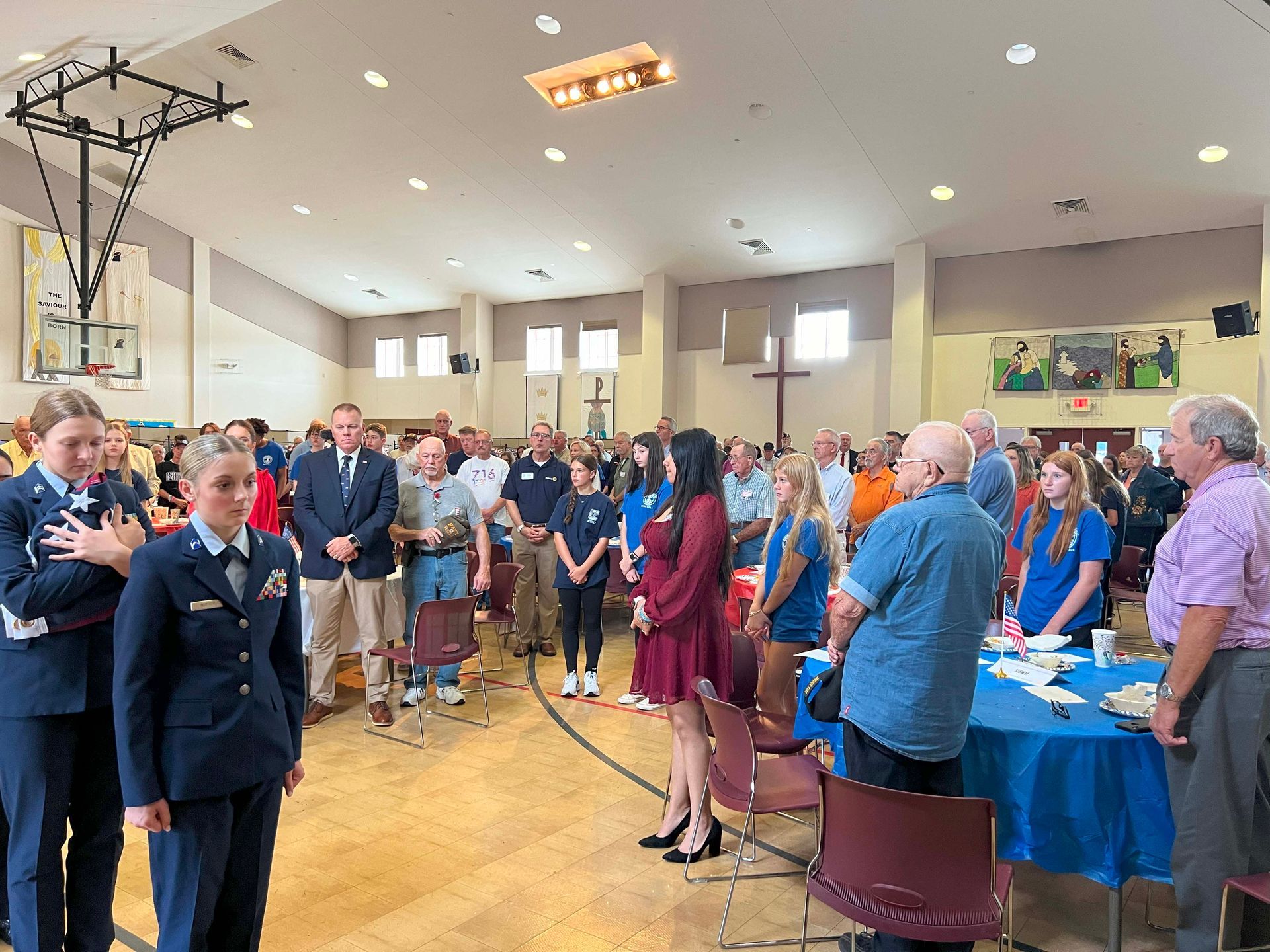 People gathered in a bright hall, standing around tables for a formal indoor event.