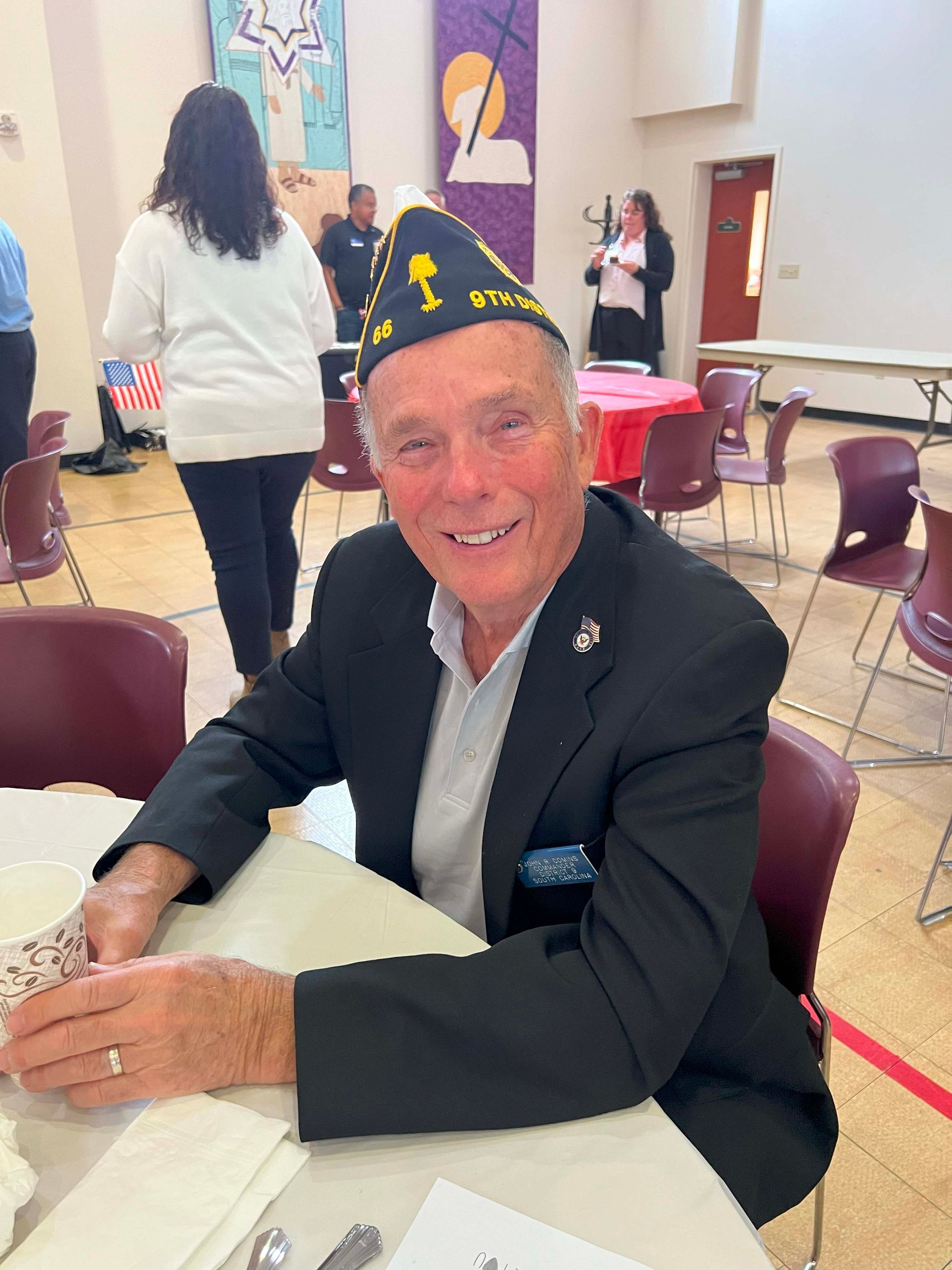 Smiling man in a black blazer and yarmulke sits at a table in a decorated room.