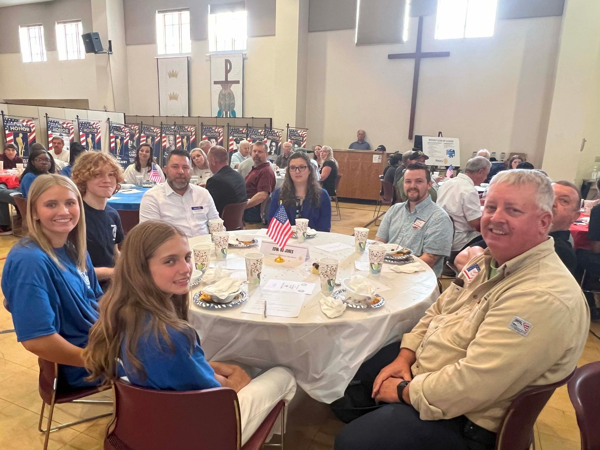 People seated at round tables in a bright hall during a community gathering