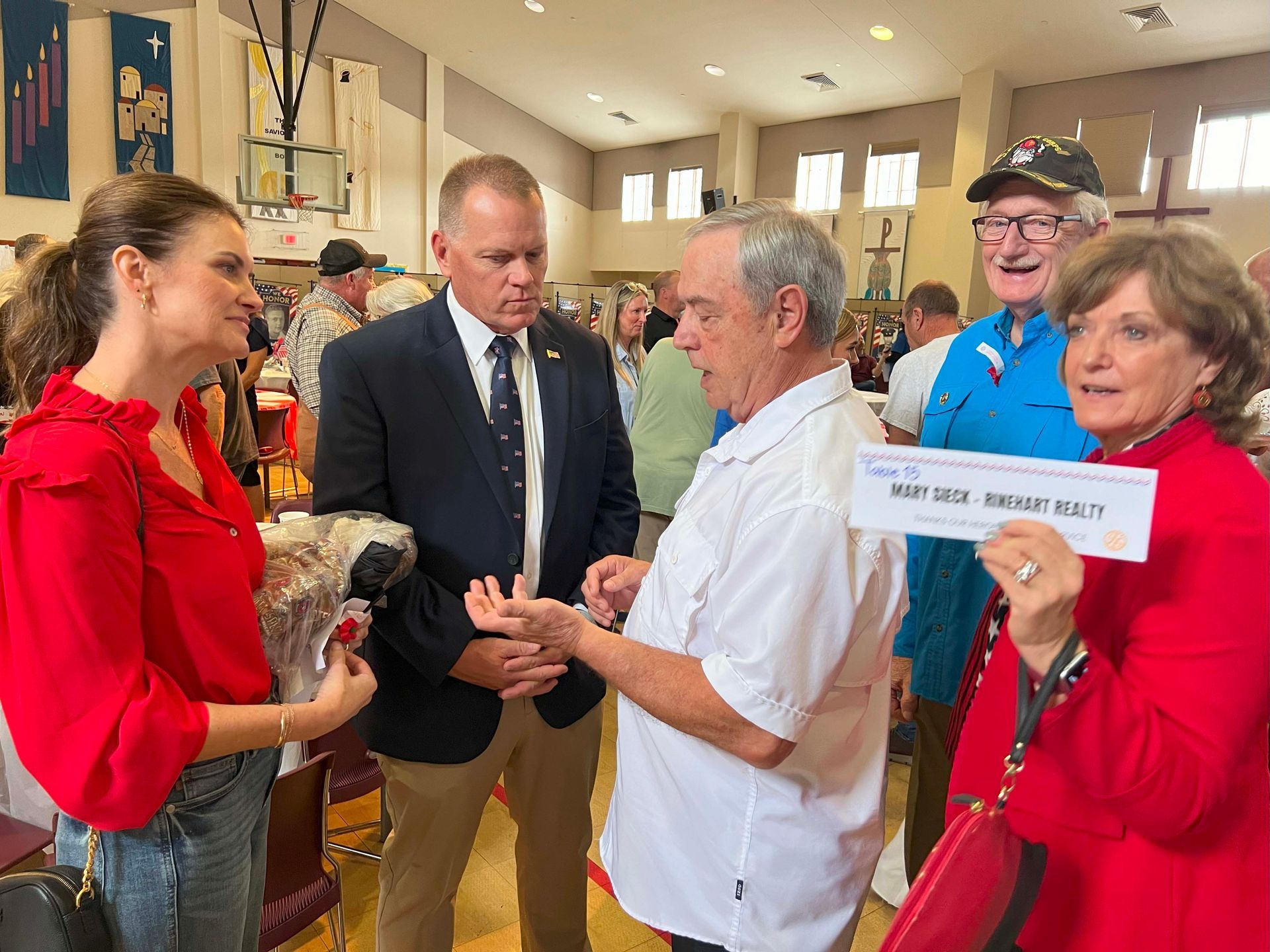 People chatting in a bright room; a woman in red holds a sign while others stand nearby.