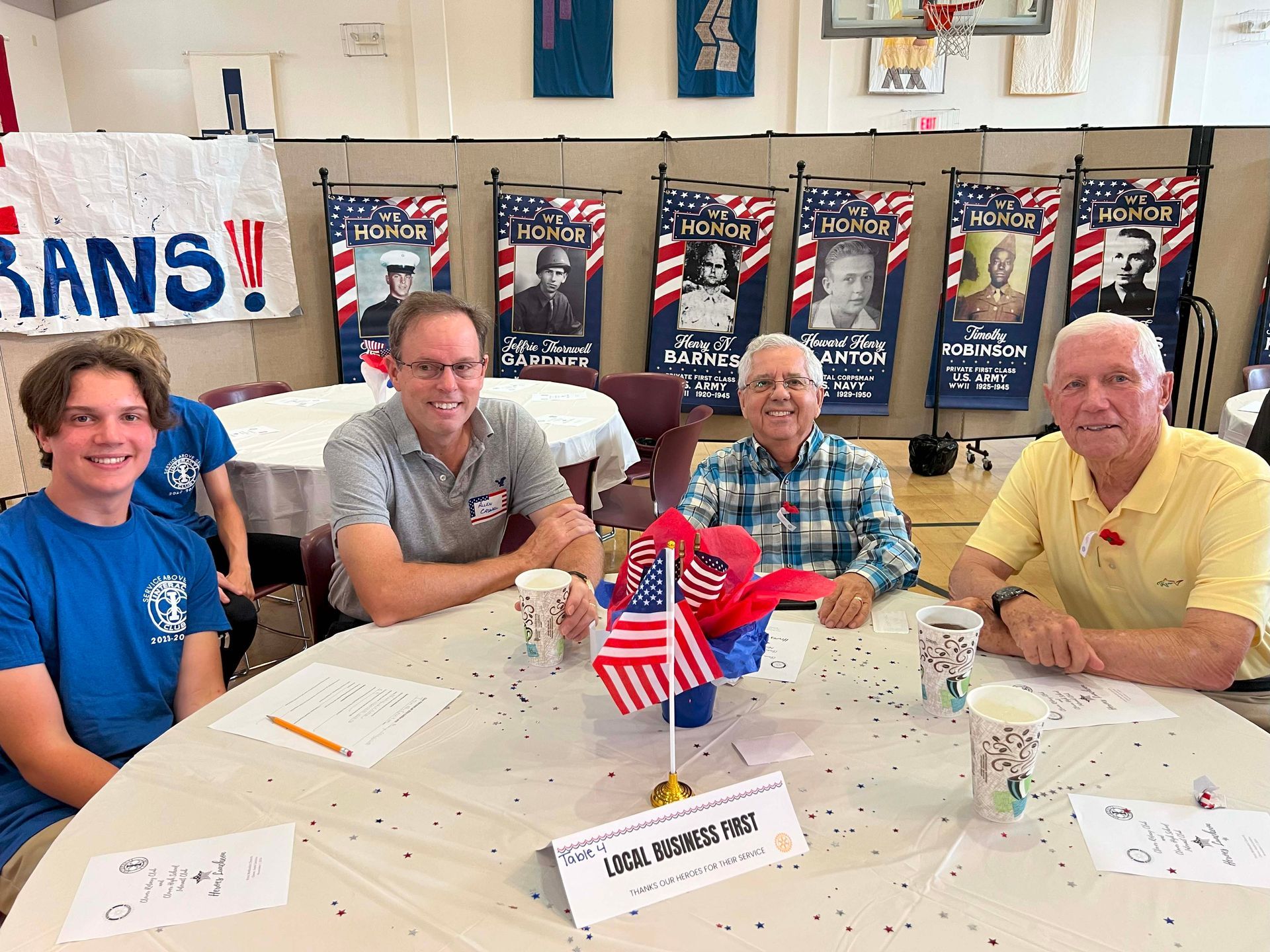 Four people seated at a table with patriotic decorations in a meeting room, smiling at the camera.