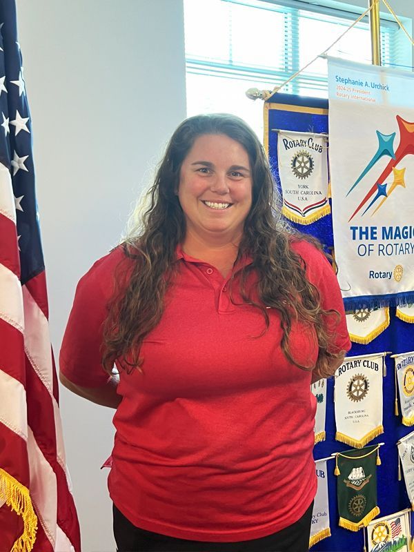 Smiling woman in red shirt standing beside banners and flags in a bright room