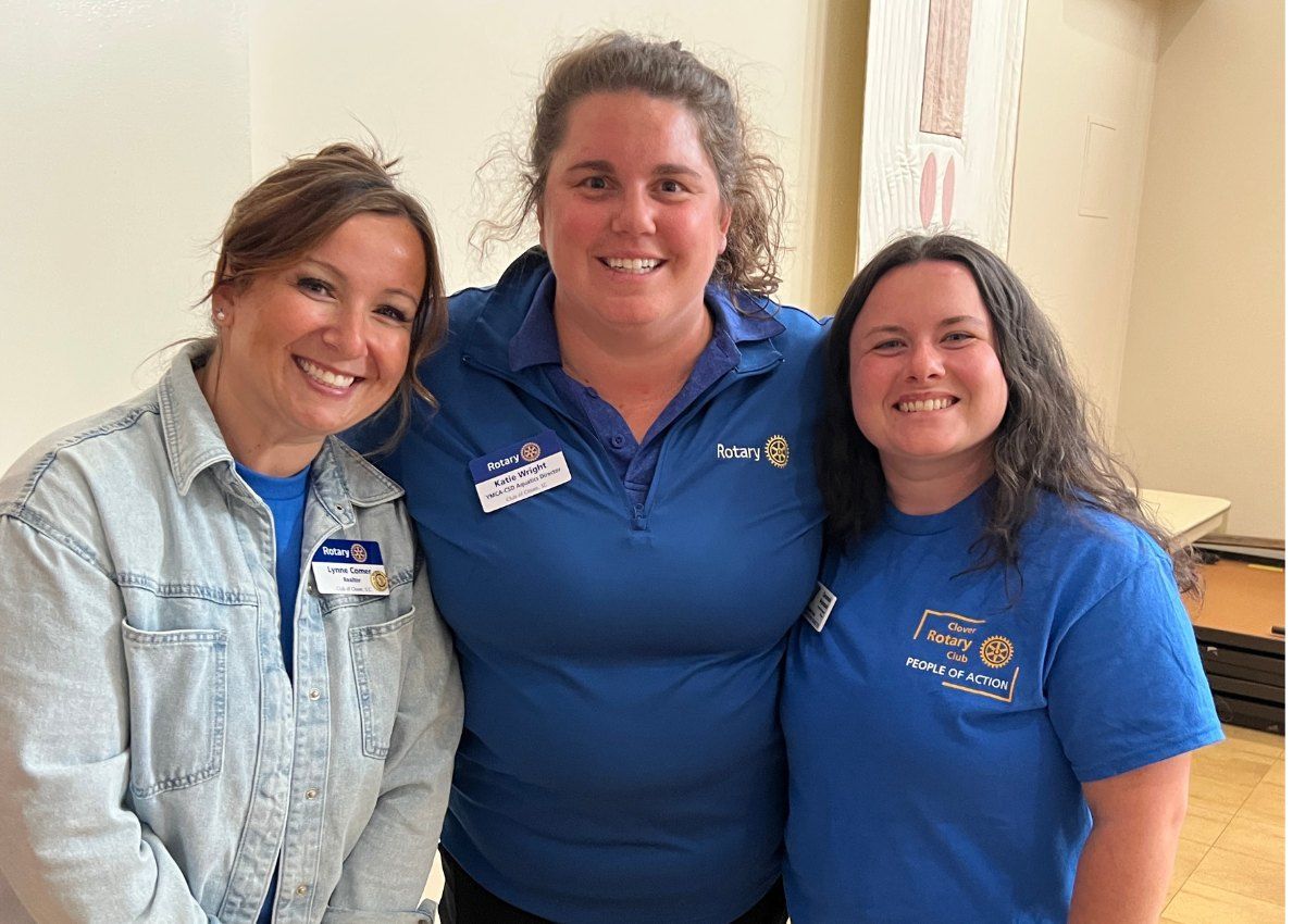 Three smiling coworkers standing indoors, wearing blue shirts and a denim jacket.