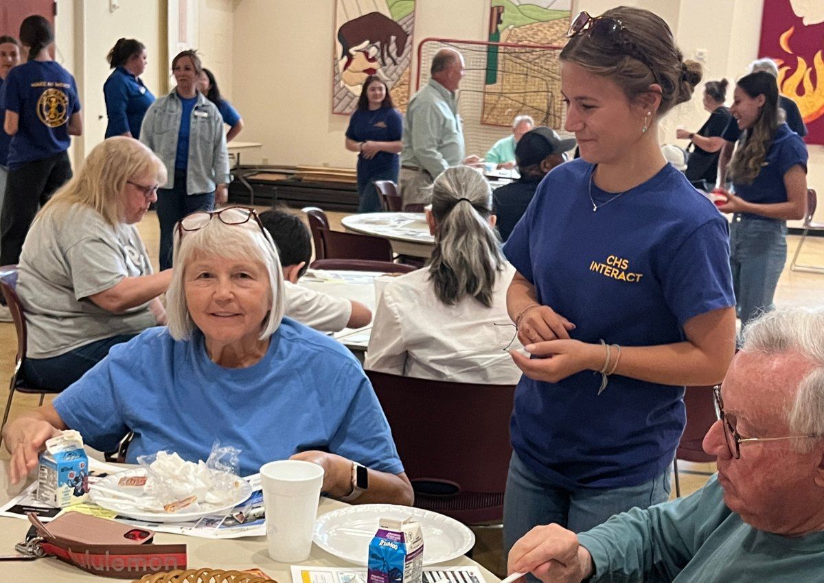Volunteers serving meals to seated guests in a busy community dining hall
