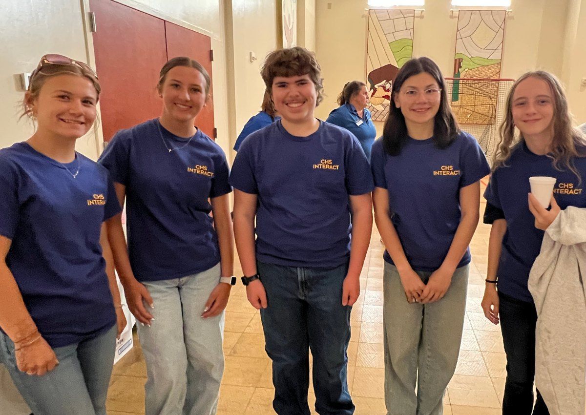 Five people in matching blue shirts stand together in a bright hallway, smiling at the camera.