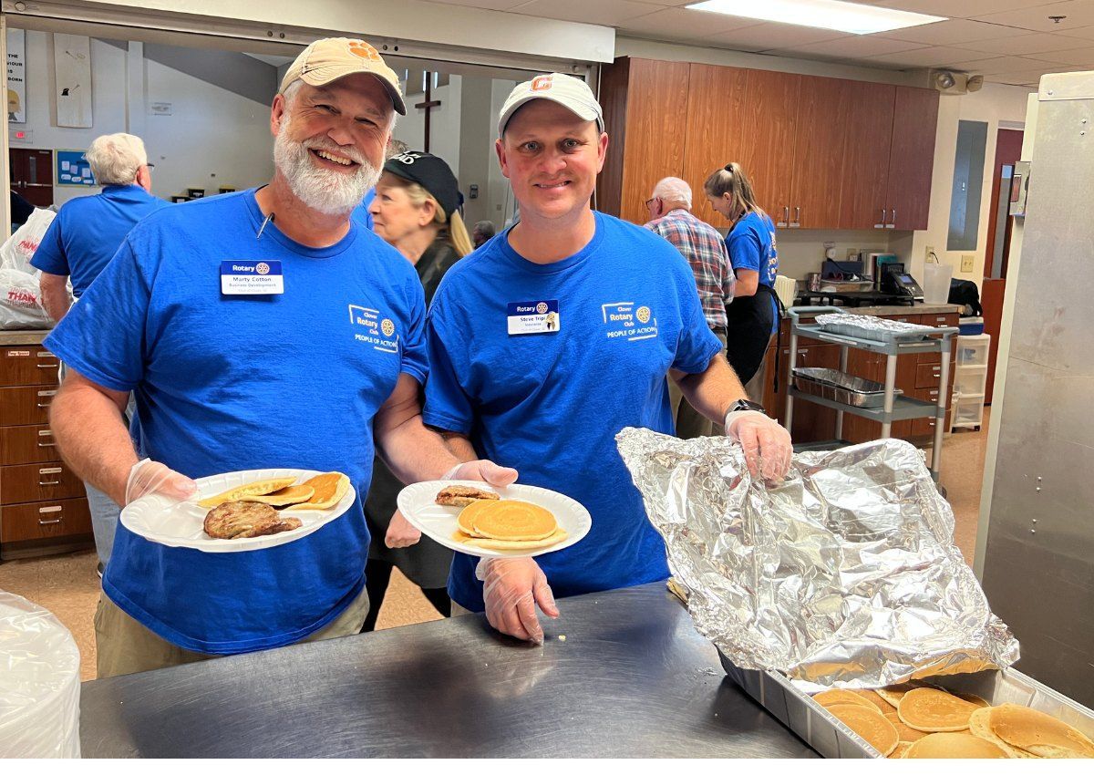 Two volunteers in blue shirts serving food at a cafeteria counter