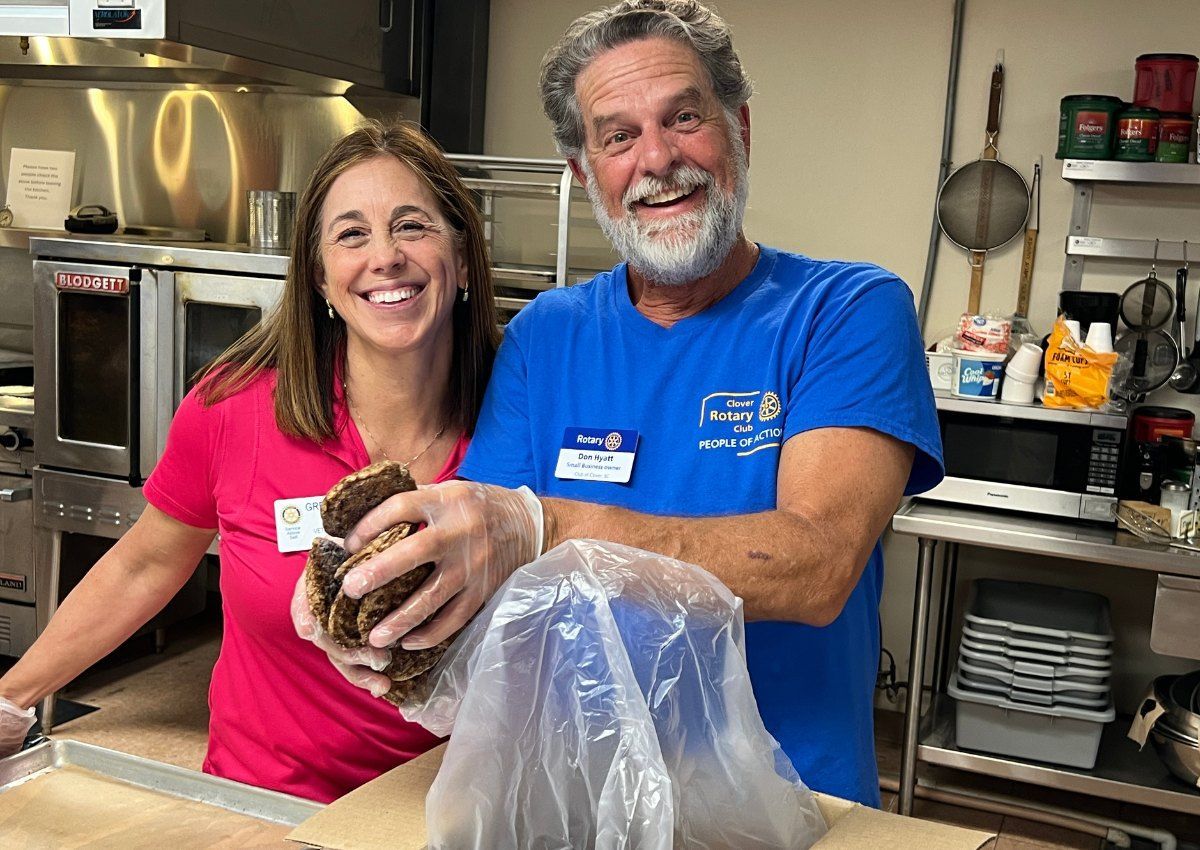 Two smiling volunteers in a kitchen holding a large shellfish, with a bag of seafood on the counter