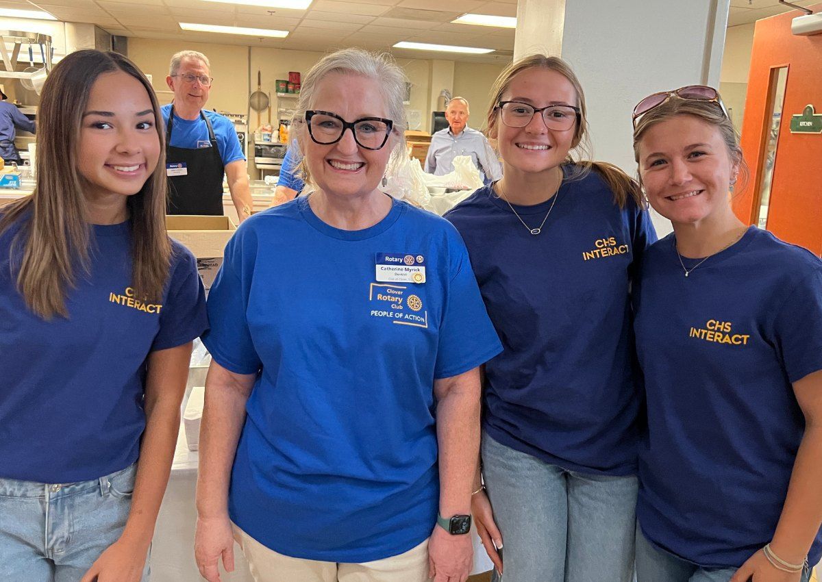 Four staff members in blue shirts smiling in a bright indoor hallway