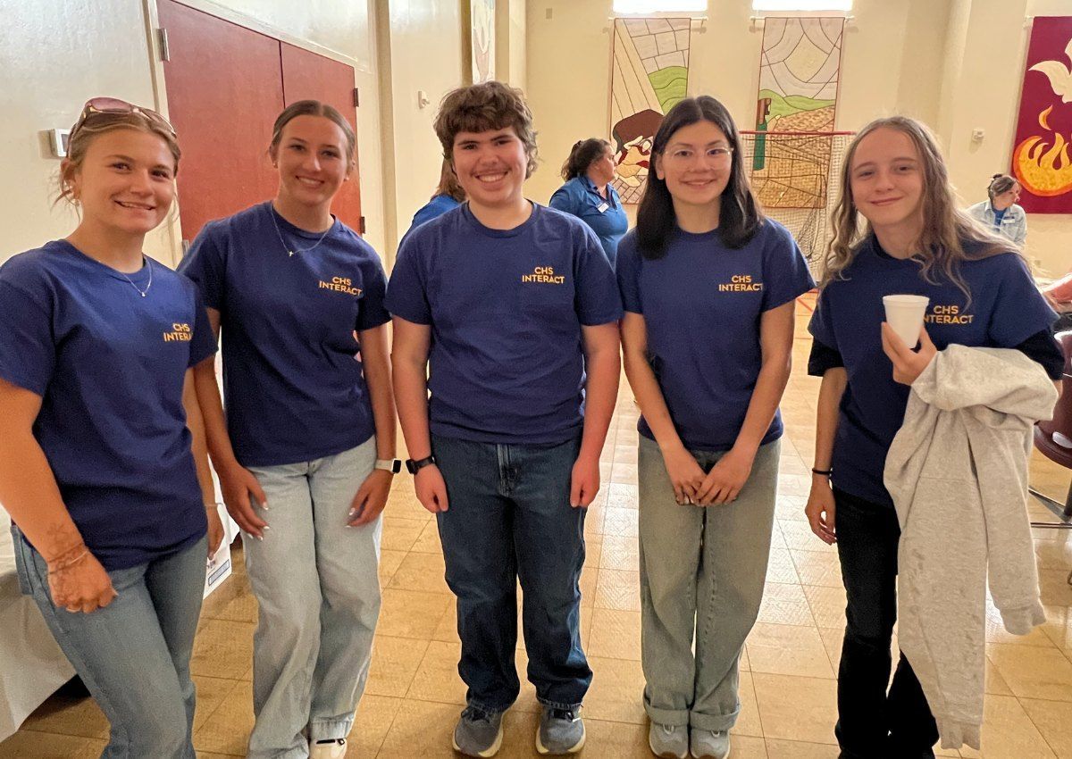 Five people in blue shirts pose together indoors, smiling in a bright hallway.