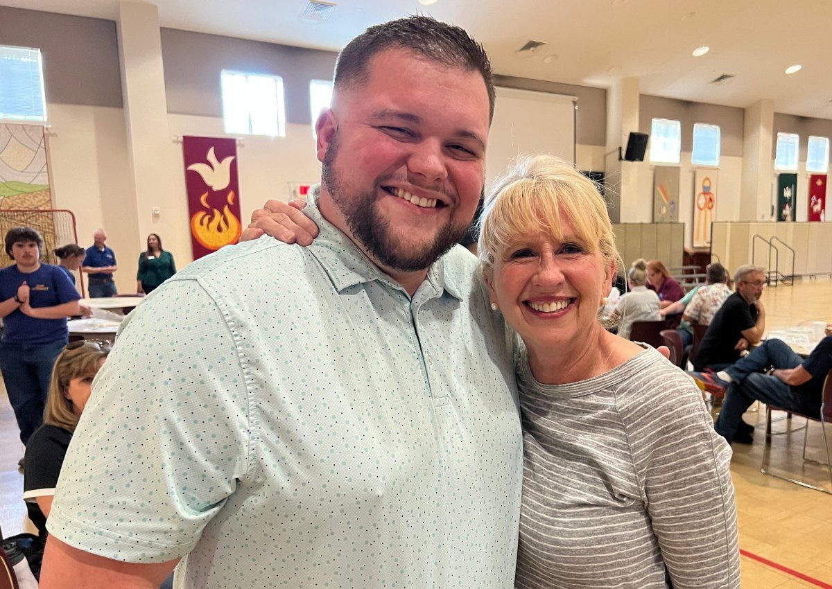 Two smiling people posing together in a gymnasium with spectators in the background