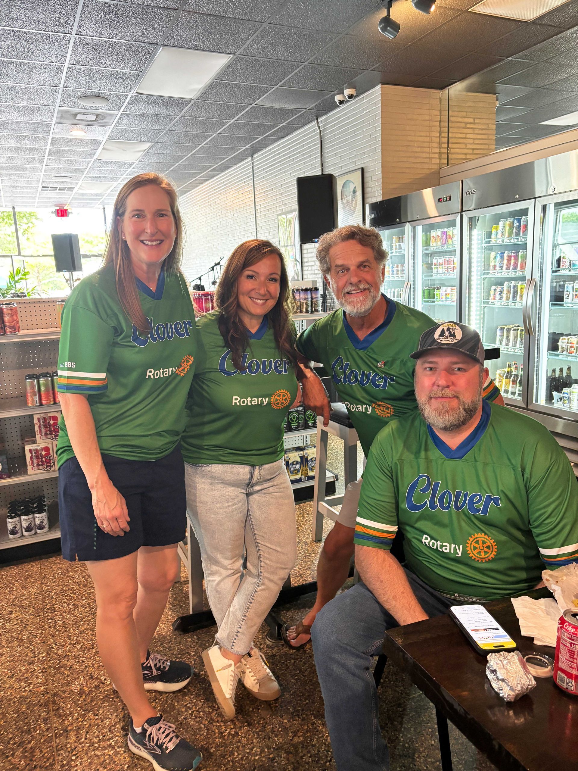 Four people in green Clover shirts posing inside a convenience store.