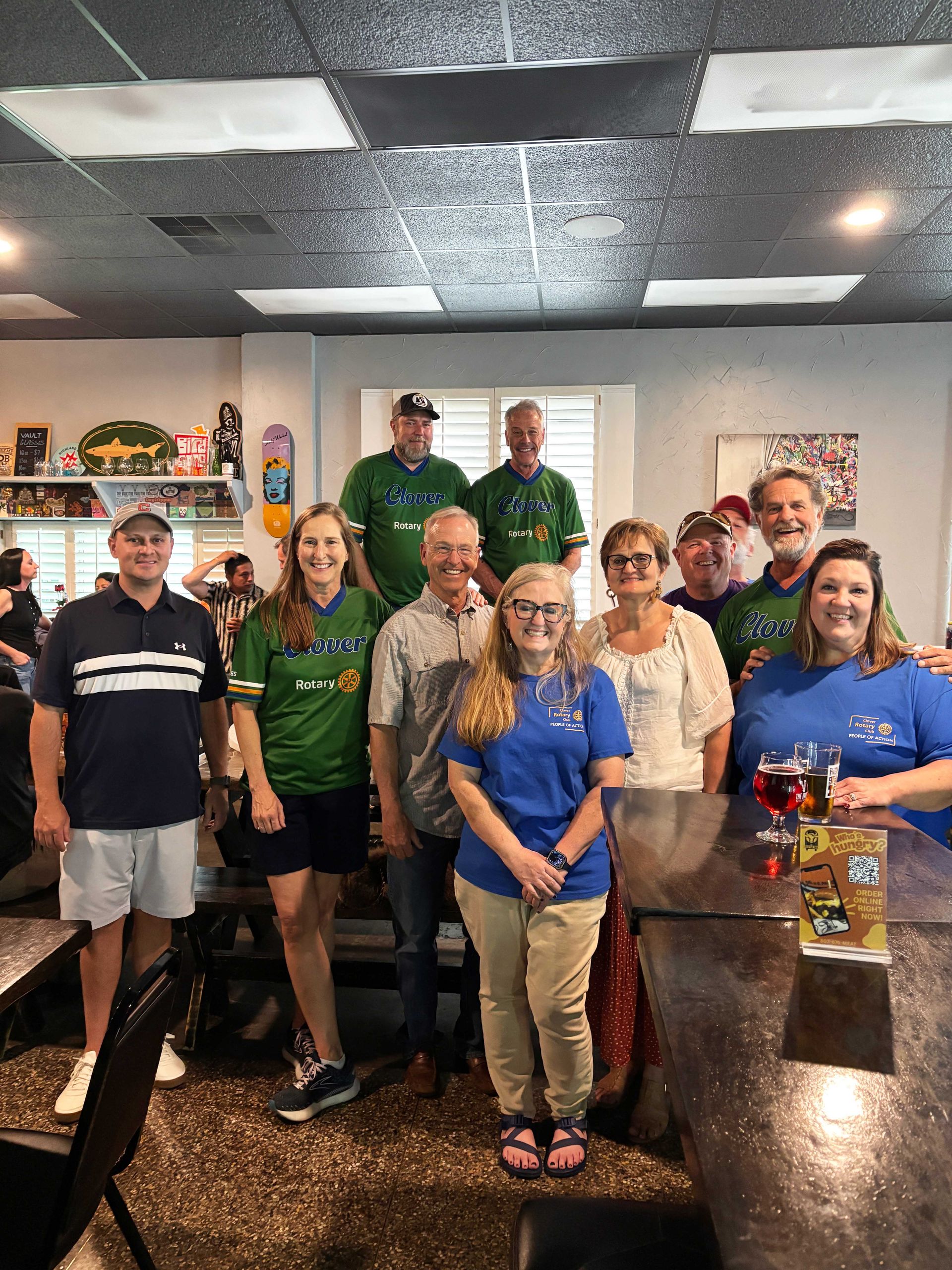 Group posing indoors in a restaurant, with smiling staff in green and blue shirts behind a counter.