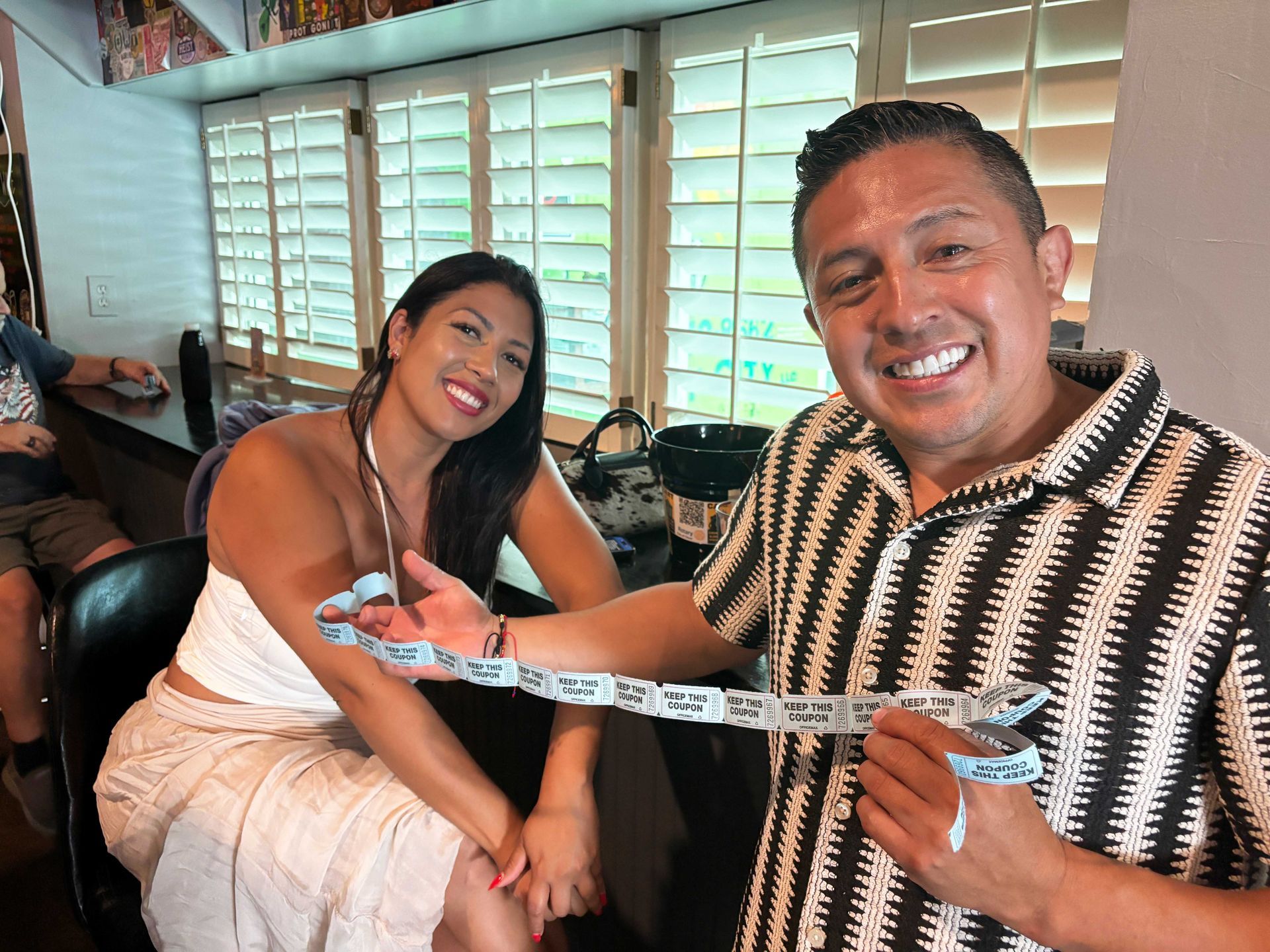 Two people smiling on a couch, holding a measuring tape between them in a bright living room.