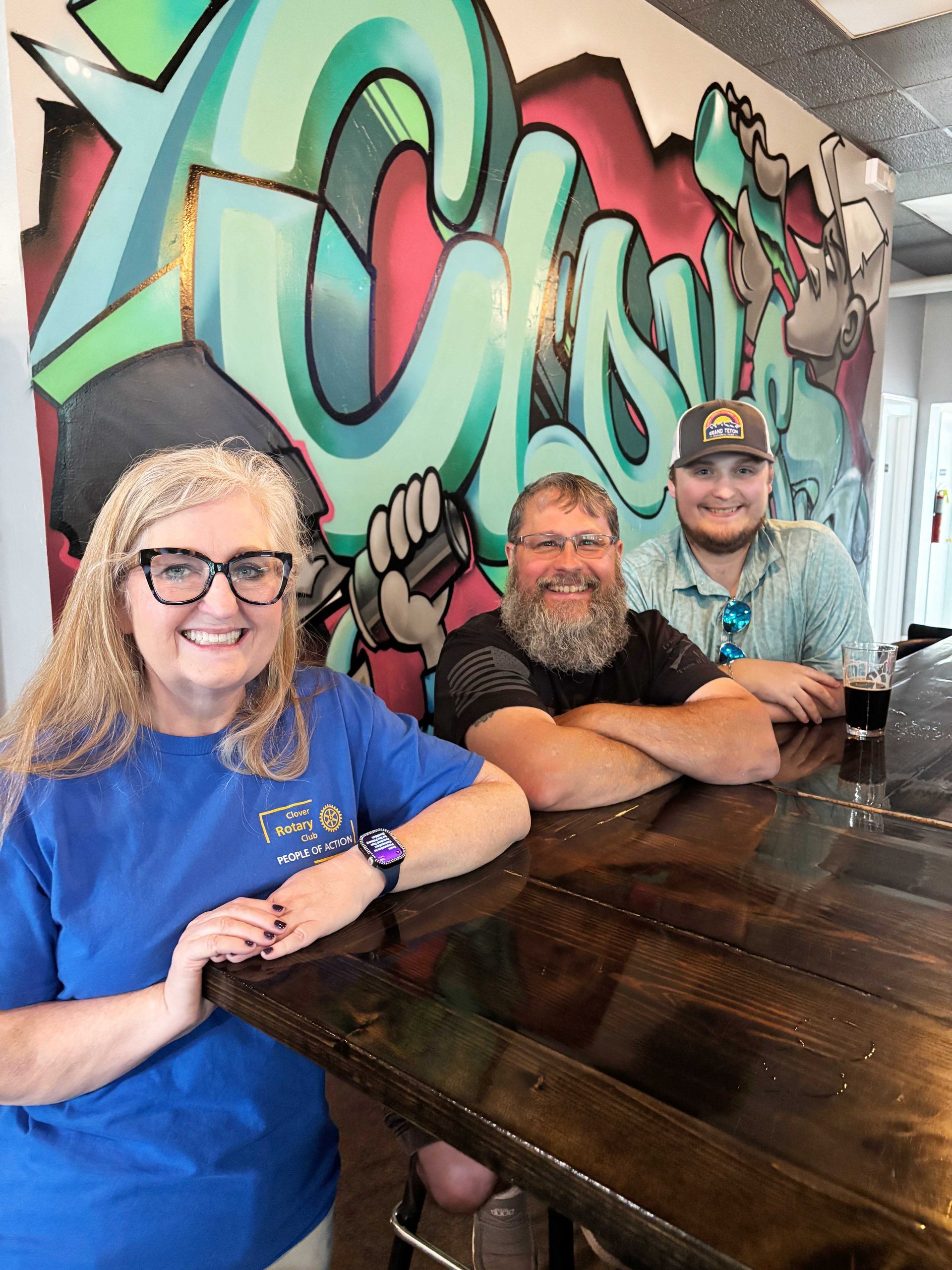 Three people smiling at a wooden table in a colorful graffiti-covered room