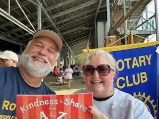 Smiling pair holding “Kindness to Share” sign at a Rotary Club event