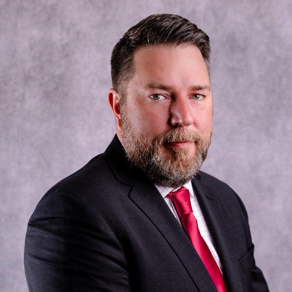 Studio portrait of a man in a dark suit and red tie against a gray backdrop