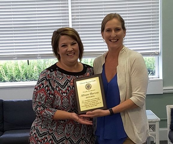 Two women holding a plaque in an office, smiling at the camera.