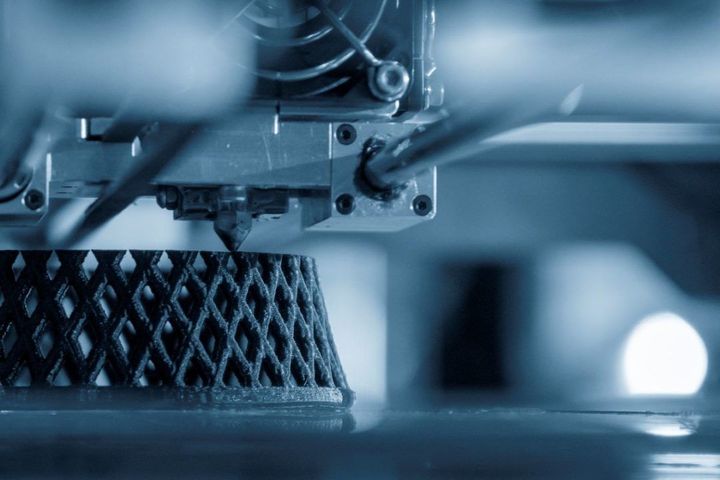 3D printer extruding a black lattice structure in a blue-lit workspace