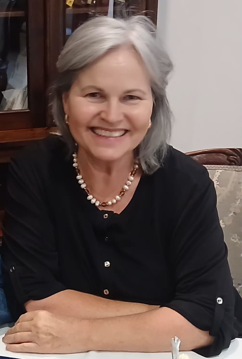 Smiling woman in an orange blouse and beige blazer, standing indoors in soft light