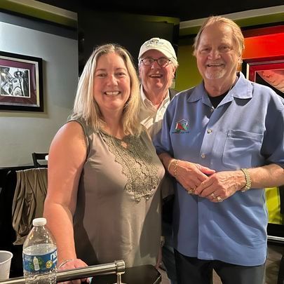 A woman is standing next to two men and a bottle of water.
