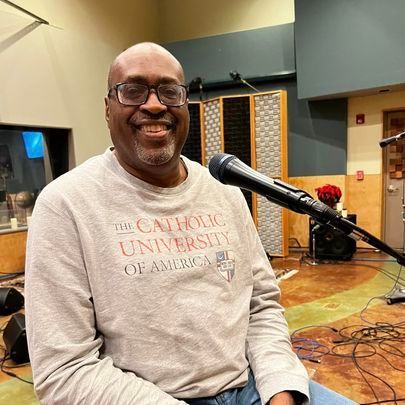 A man is sitting in front of a microphone in a recording studio.