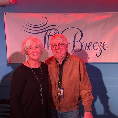 A man and a woman are posing for a picture in front of a breeze sign.