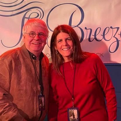 A man and a woman are posing for a picture in front of a breeze sign.
