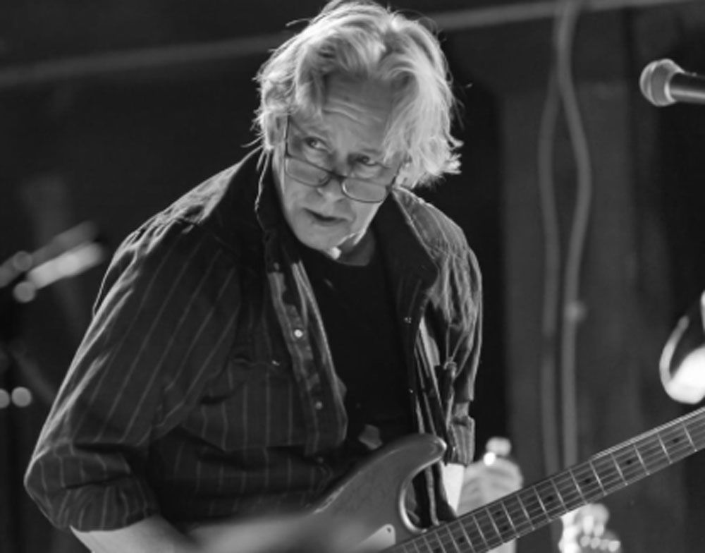 A man with glasses is playing a guitar in a black and white photo
