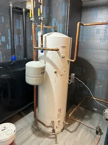 White water heater tank with copper pipes, pressure tank, and black tank in a basement.