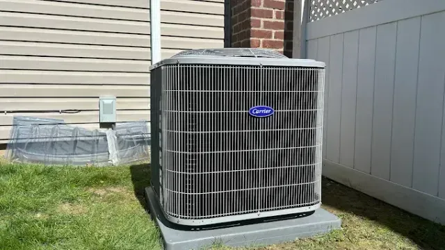 Carrier air conditioning unit outside a building with siding, next to a brick wall and a white fence.