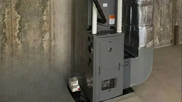 Furnace in a concrete-walled room, with metal ductwork and pipes, and a small pump.