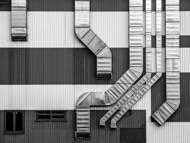 Black and white photo of corrugated building exterior with industrial ductwork.