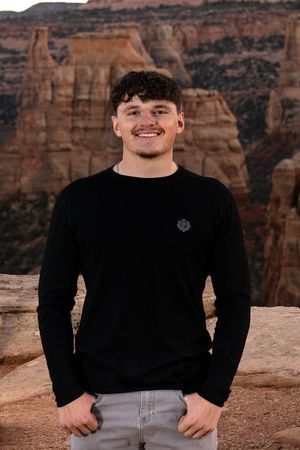 Smiling person in a black shirt standing in front of a rocky canyon wall.
