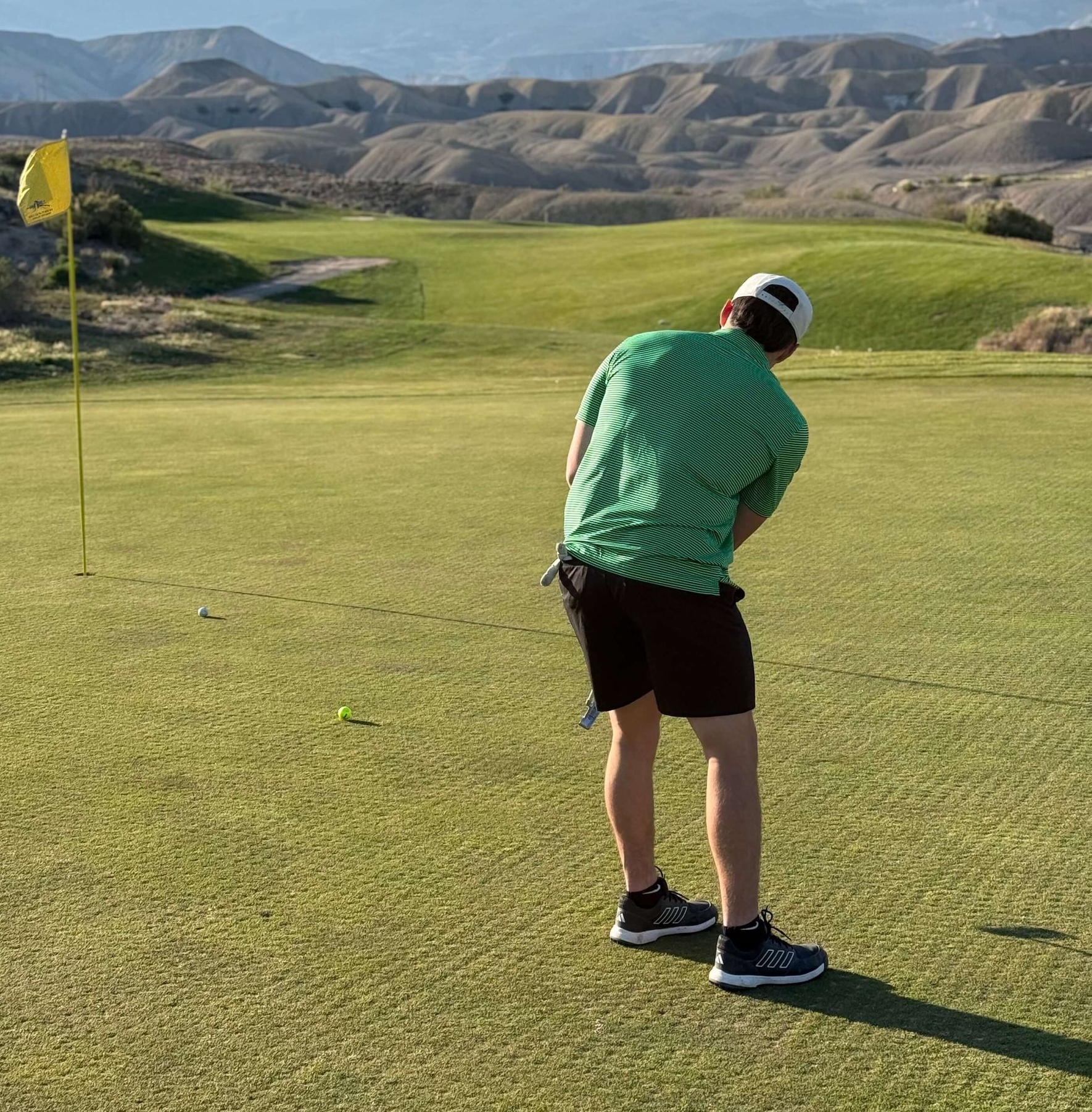 Golfer in a green striped shirt putting on a course with mountains in the background