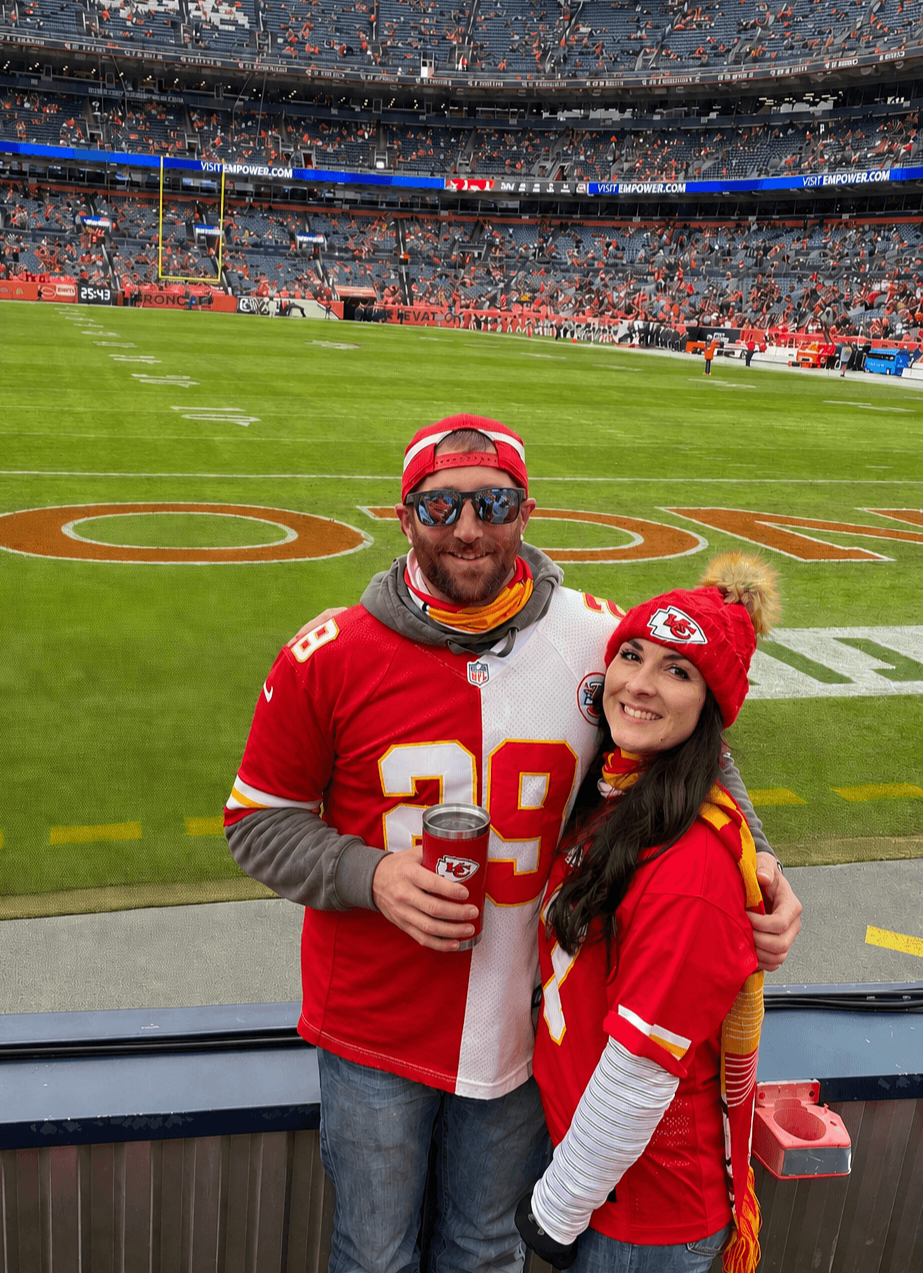 Couple in red Kansas City Chiefs gear posing at a football stadium field sideline