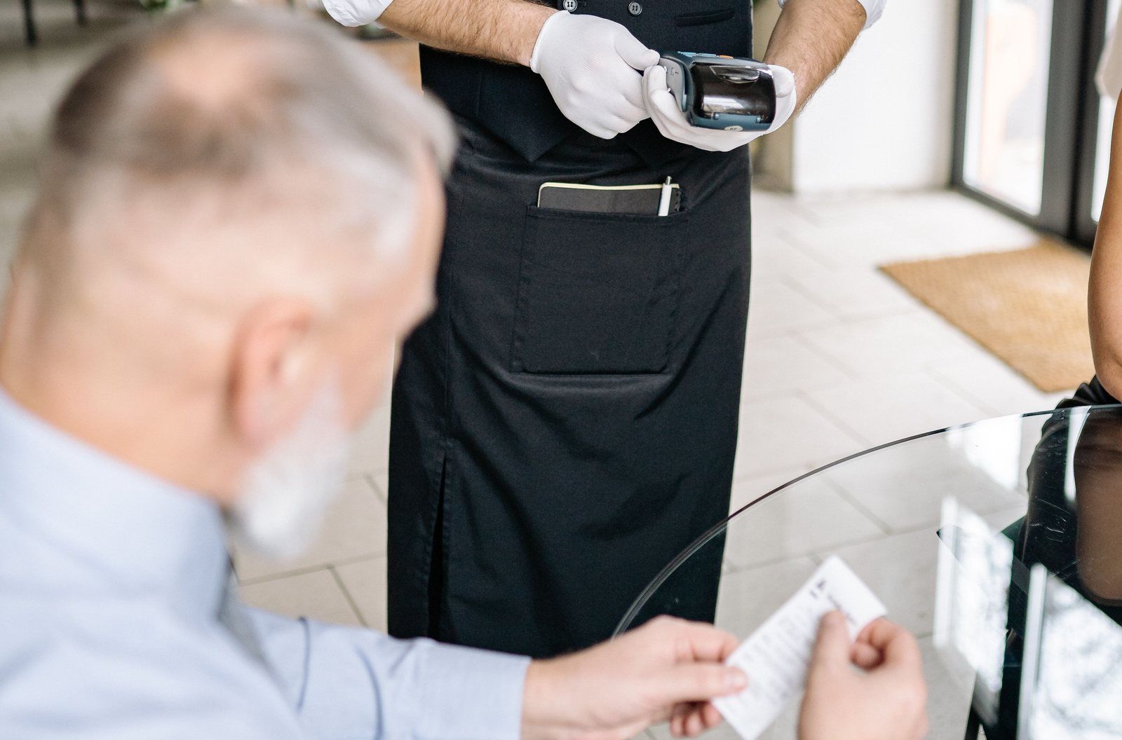 Server holding a handheld card reader while a seated guest reviews the receipt at a restaurant table