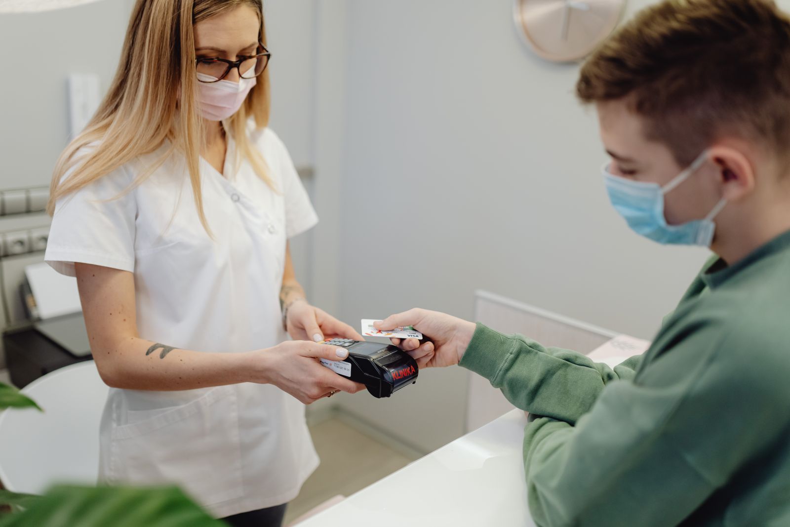 Medical office worker in scrubs holding a card reader for a patient paying with a credit card